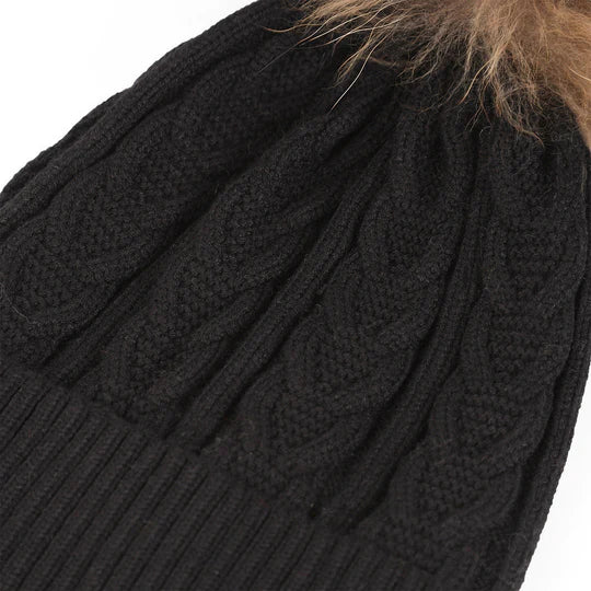 Snuggyz cable-knit black and natural pom pom beanie with a cozy, stylish design, perfect for cold weather accessories.