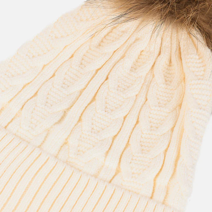 Snuggyz cable-knit pom pom beanie in ice white with natural accents, cozy winter accessory for cold weather.