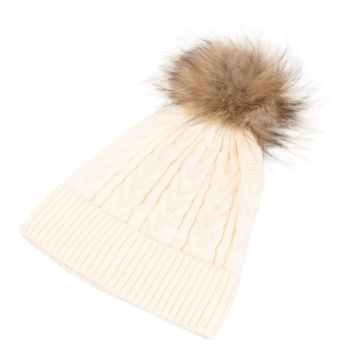 Snuggyz cable-knit pom pom beanie in ice white and natural colors, cozy winter accessory with a fluffy pom pom on top.